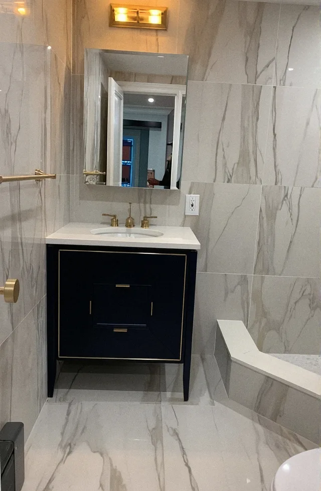 Bathroom after the remodel, marble tile with a navy vanity and brass fixtures